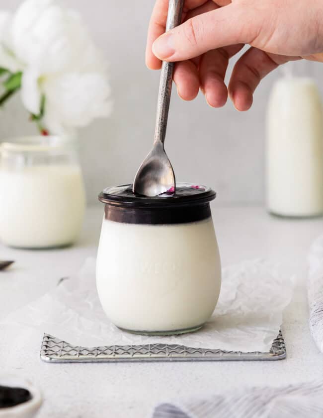 plunging a spoon into vanilla panna cotta in a jar with chocolate on top.