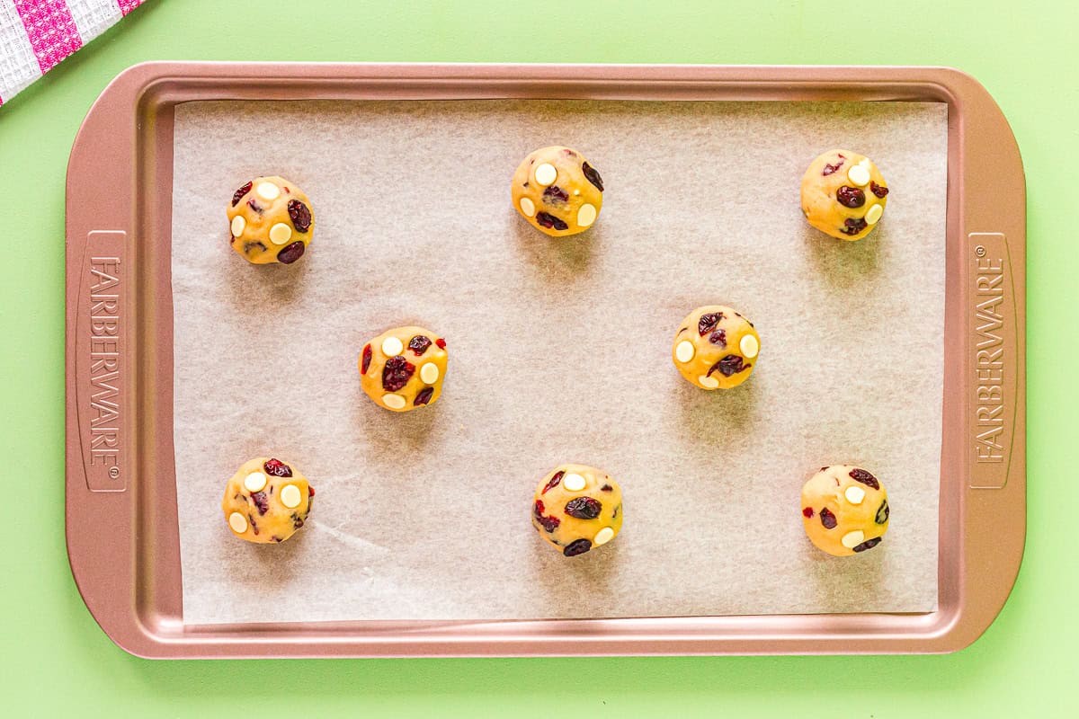 8 white chocolate cranberry cookie dough balls on a baking sheet.