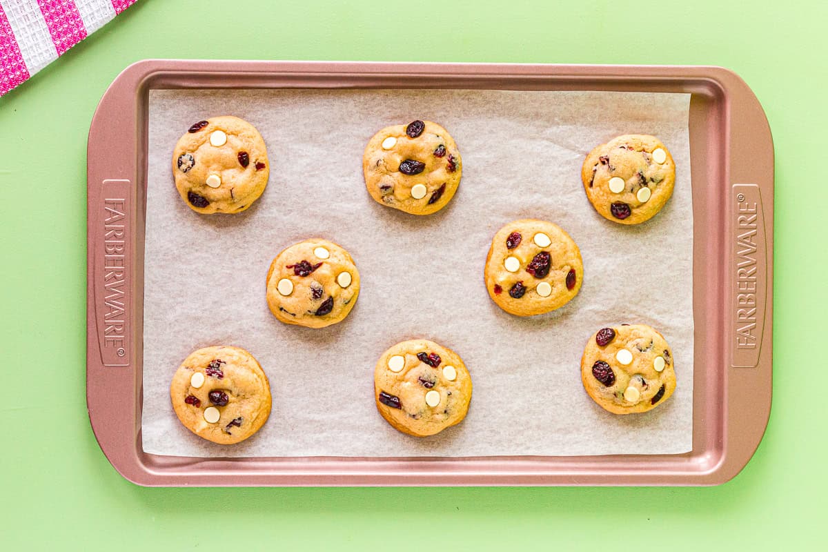 8 baked white chocolate cranberry cookies on a lined baking sheet.