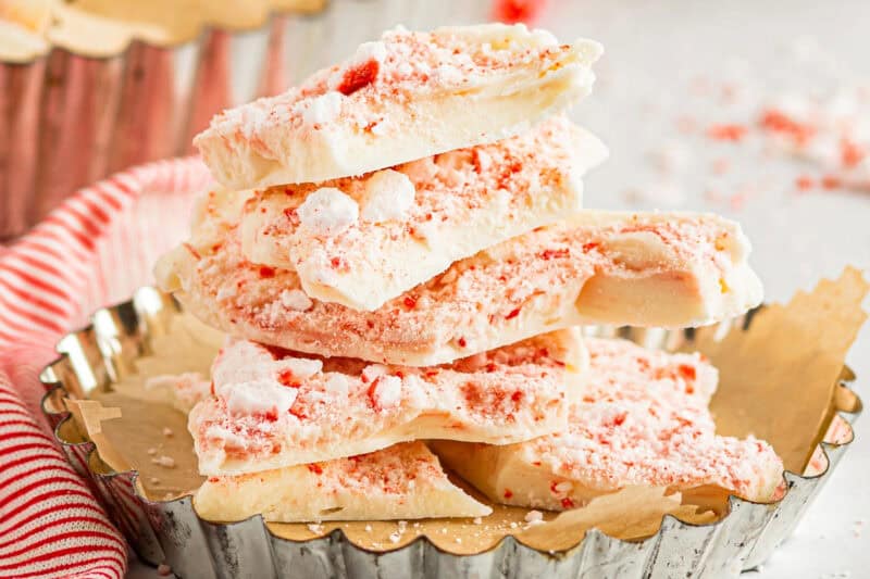 side view view of stacked broken white chocolate peppermint bark pieces in a parchment-lined tart pan.