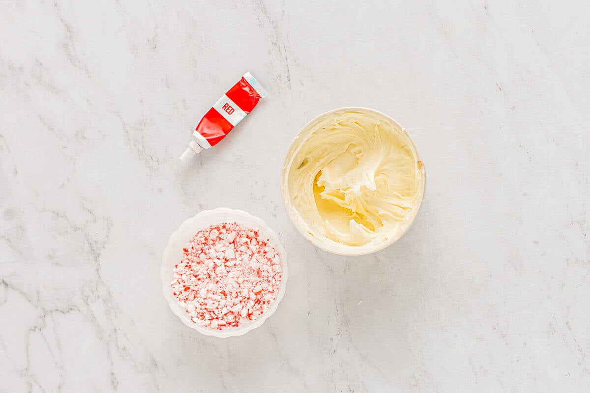 melted peppermint white chocolate in a bowl next to crushed candy canes and red food coloring.