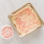 red food coloring swirled into melted white chocolate in a parchment-lined square baking pan.