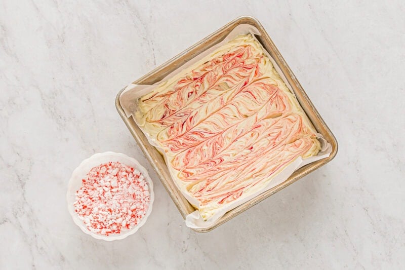 red food coloring swirled into melted white chocolate in a parchment-lined square baking pan.