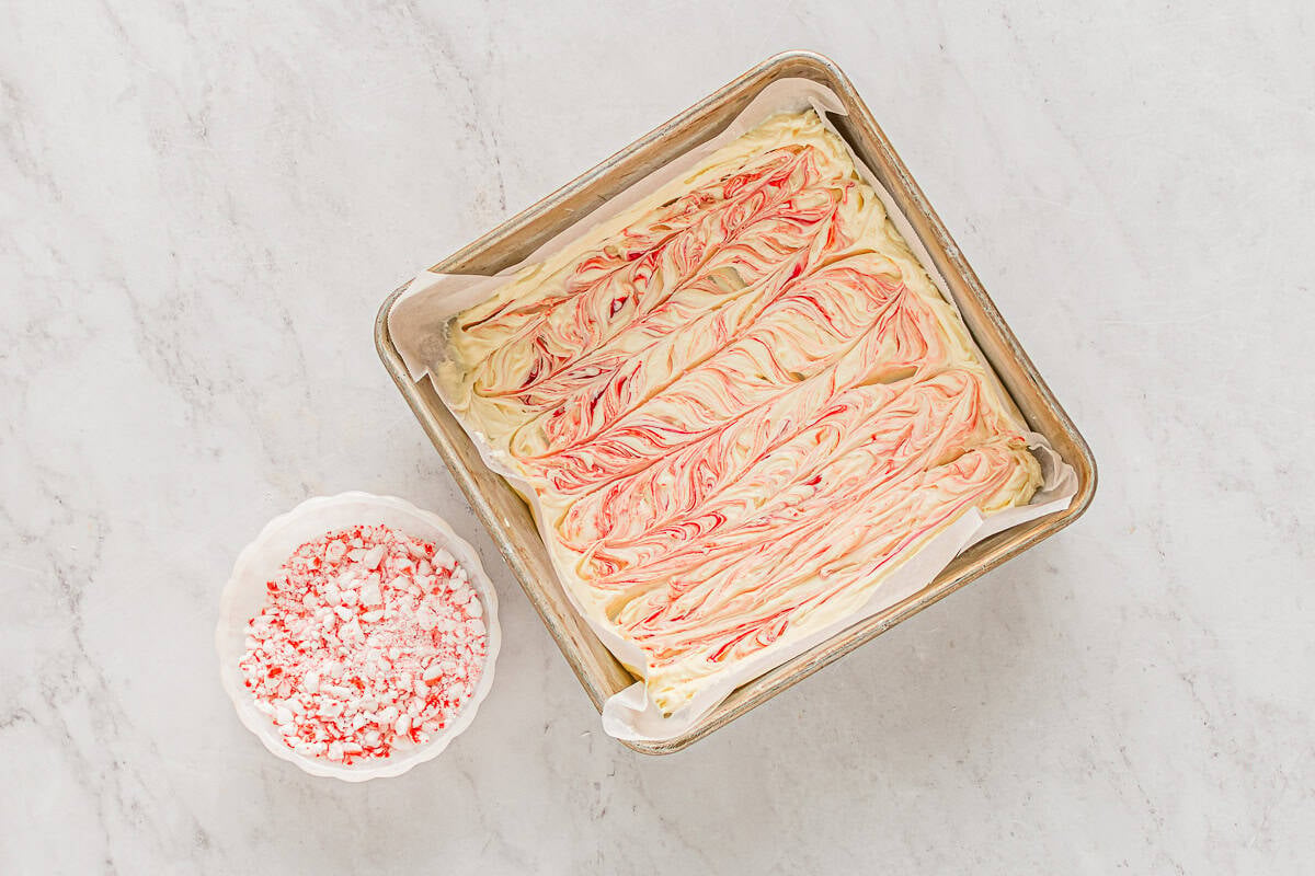red food coloring swirled into melted white chocolate in a parchment-lined square baking pan.