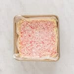 crushed peppermints over top of white chocolate peppermint bark in a parchment-lined square baking pan.