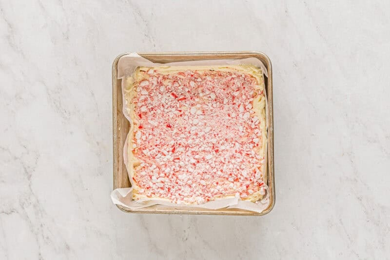 crushed peppermints over top of white chocolate peppermint bark in a parchment-lined square baking pan.