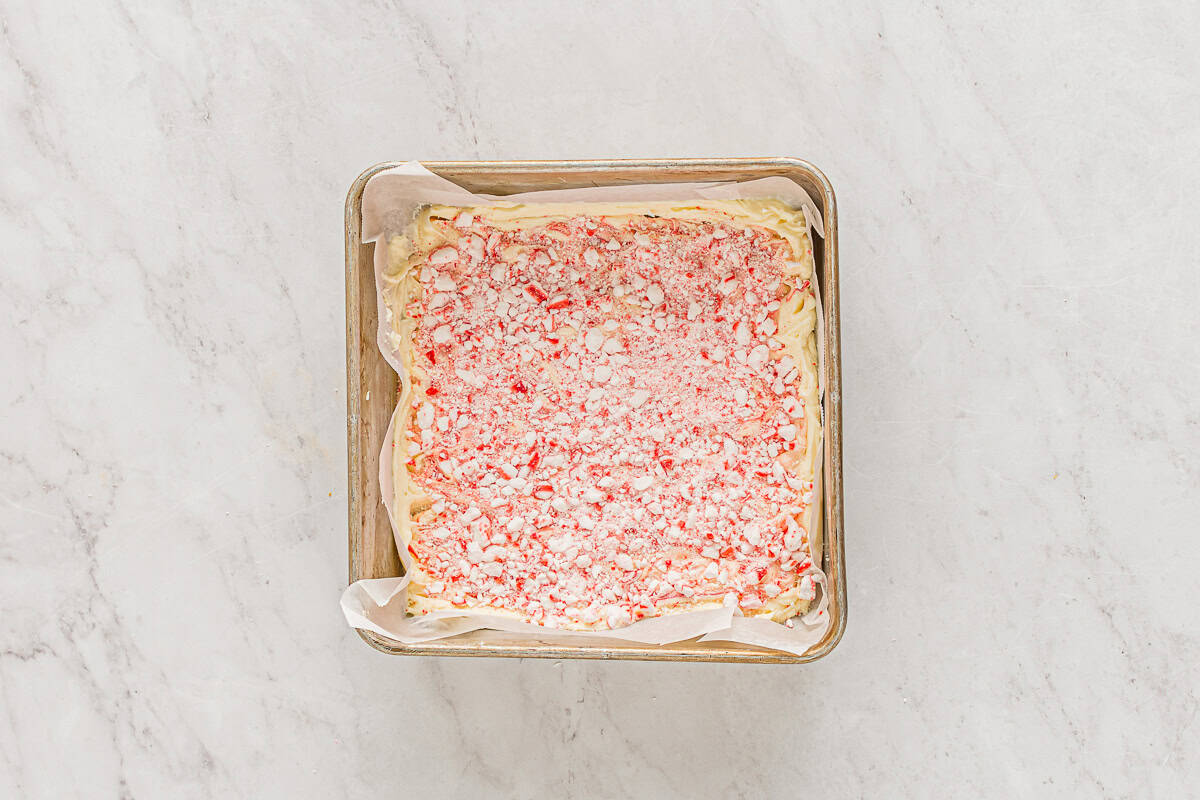 crushed peppermints over top of white chocolate peppermint bark in a parchment-lined square baking pan.