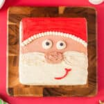 cropped overhead view of frosted santa face cake on a wooden cutting board.
