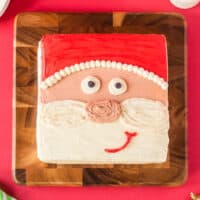 cropped overhead view of frosted santa face cake on a wooden cutting board.