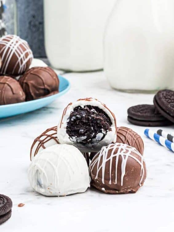 a pile of oreo truffles, one on top has a bite taken out to reveal the cookie center