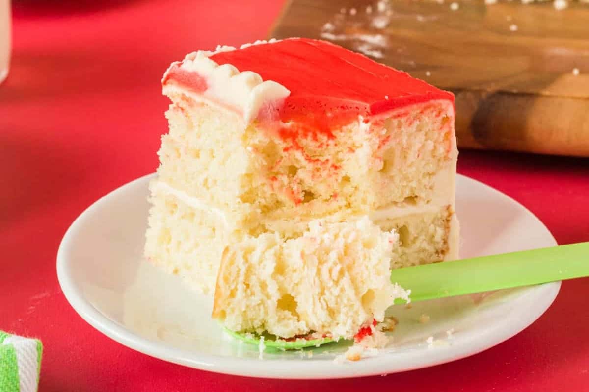 side view of a partially eaten slice of peppermint santa cake on a white plate with a green fork.