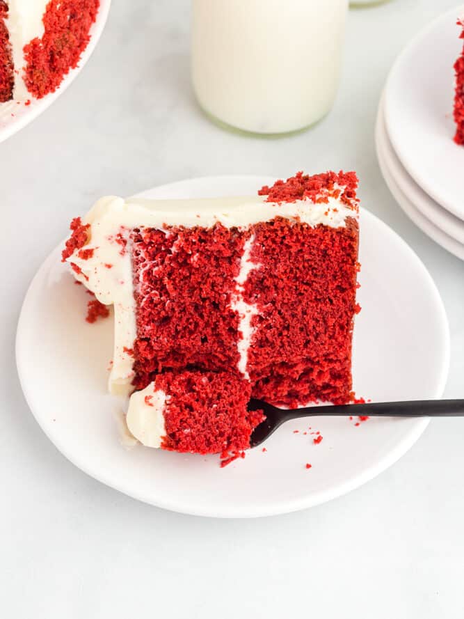 a partially eaten slice of red velvet cake on a white plate with a fork.