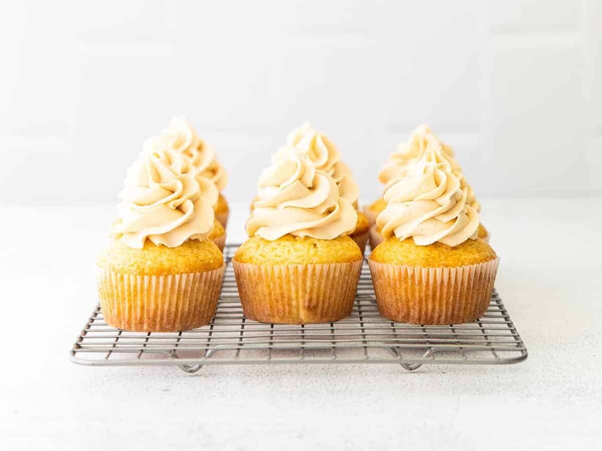 caramel cupcakes with buttercream frosting lined up on a cooling rack