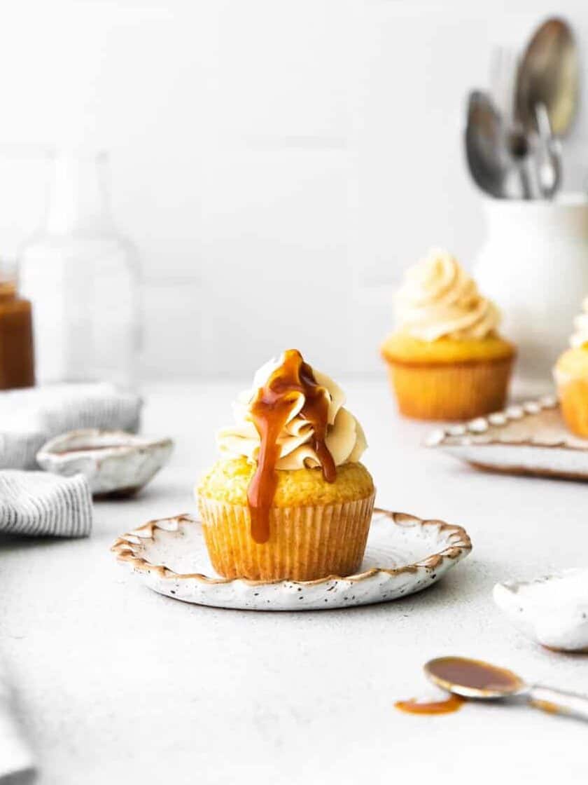 salted caramel cupcake topped with caramel drizzle at the center, with more cupcakes, a jar of caramel in the background