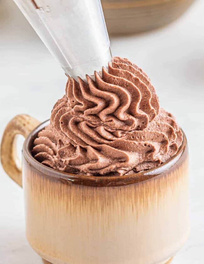 piping chocolate whipped cream frosting into a mug