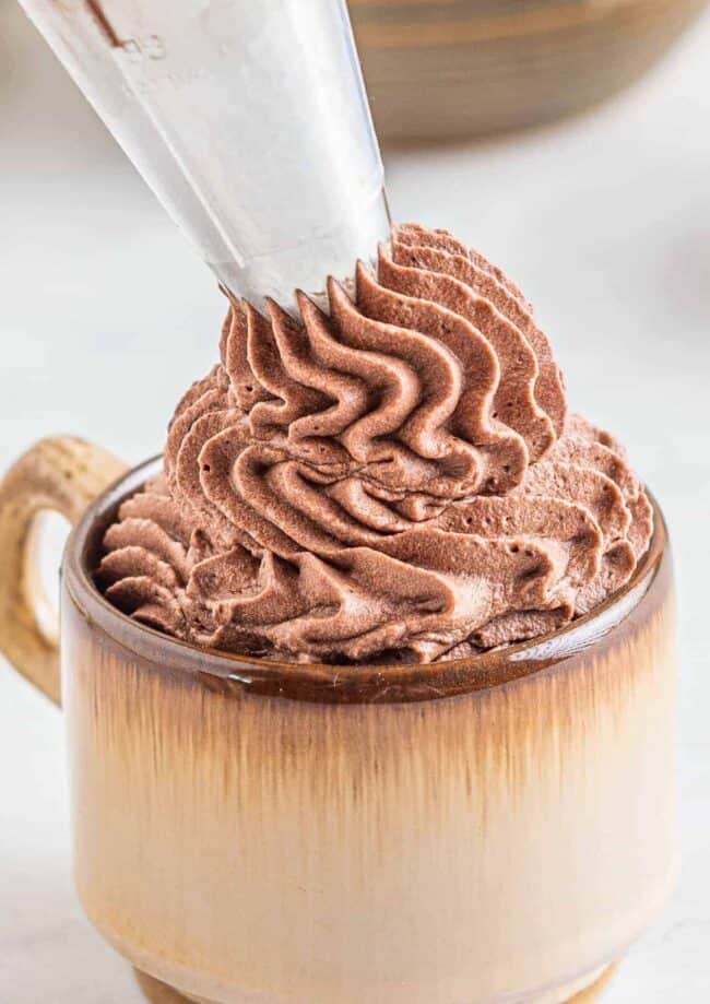 piping chocolate whipped cream frosting into a mug