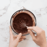 whisking bloomed cocoa powder and milk in a glass bowl with a whisk.