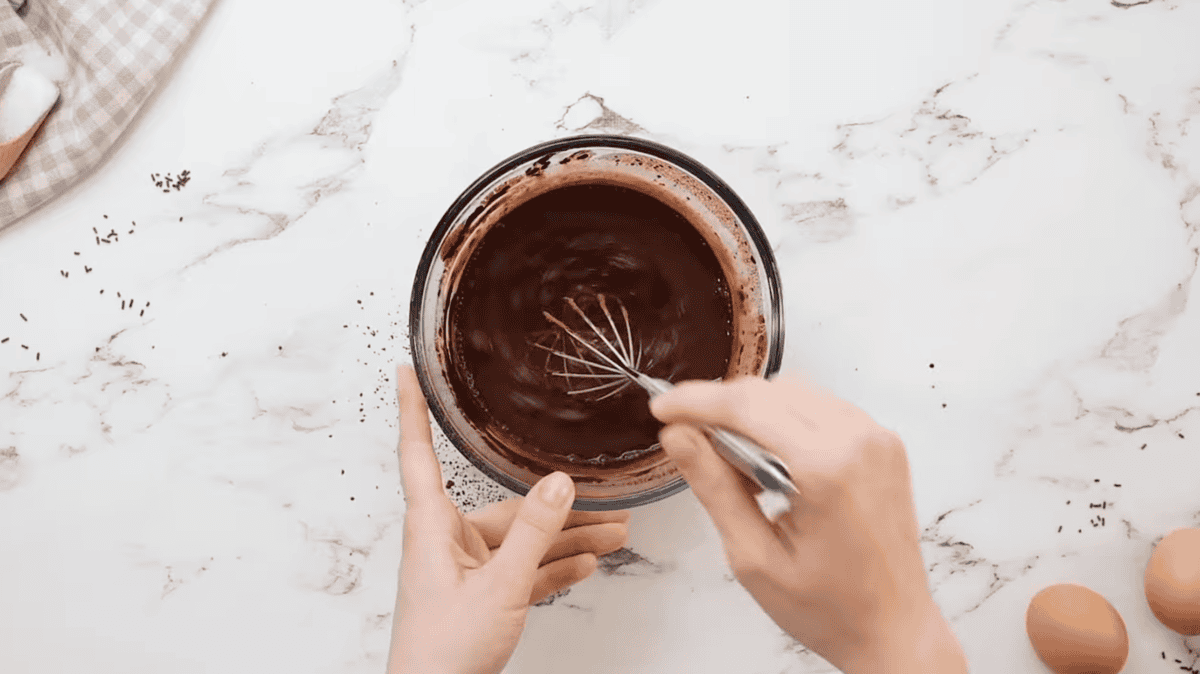 whisking bloomed cocoa powder and milk in a glass bowl with a whisk.