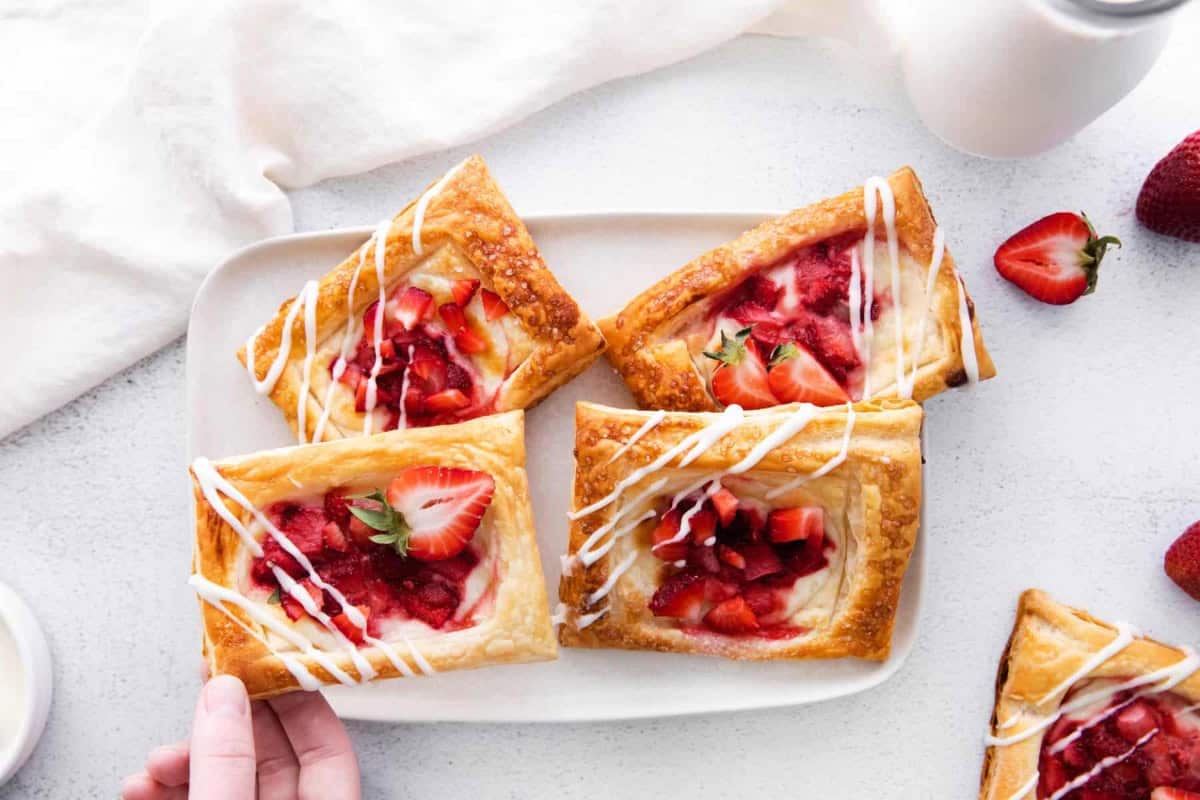 grabbing a strawberry danish from a plate with 4 danishes.