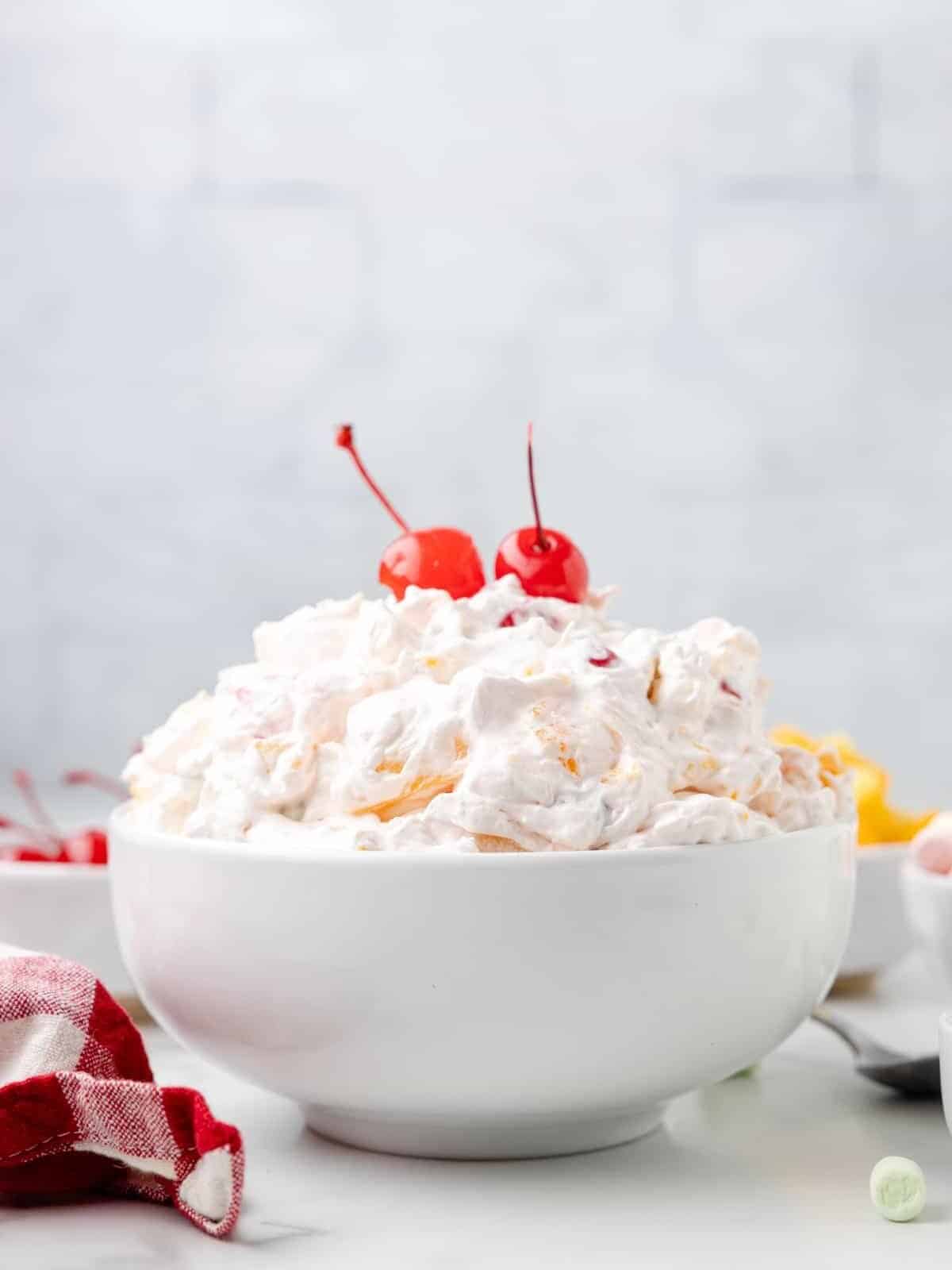 side view of classic ambrosia salad in a white bowl with 2 maraschino cherries on top.
