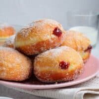 side view of 5 brioche donuts filled with raspberry jam on a pink plate.