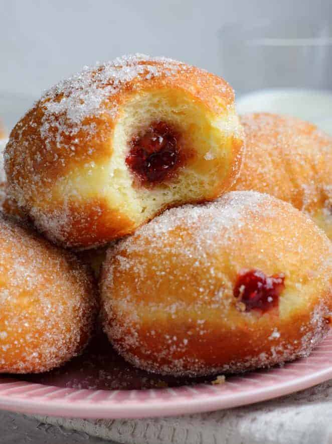 close up side view of brioche donuts filled with raspberry jam on a pink plate, the top one has been bitten.