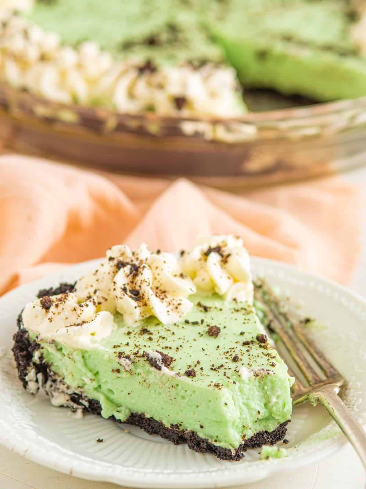 three-quarters view of a partially eaten slice of grasshopper pie on a white plate with a fork.