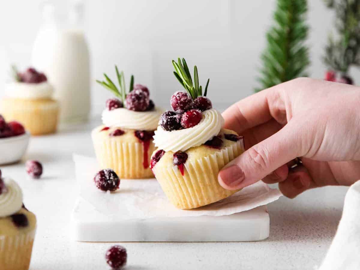 hand grabbing a cupcake topped with sugared cranberries