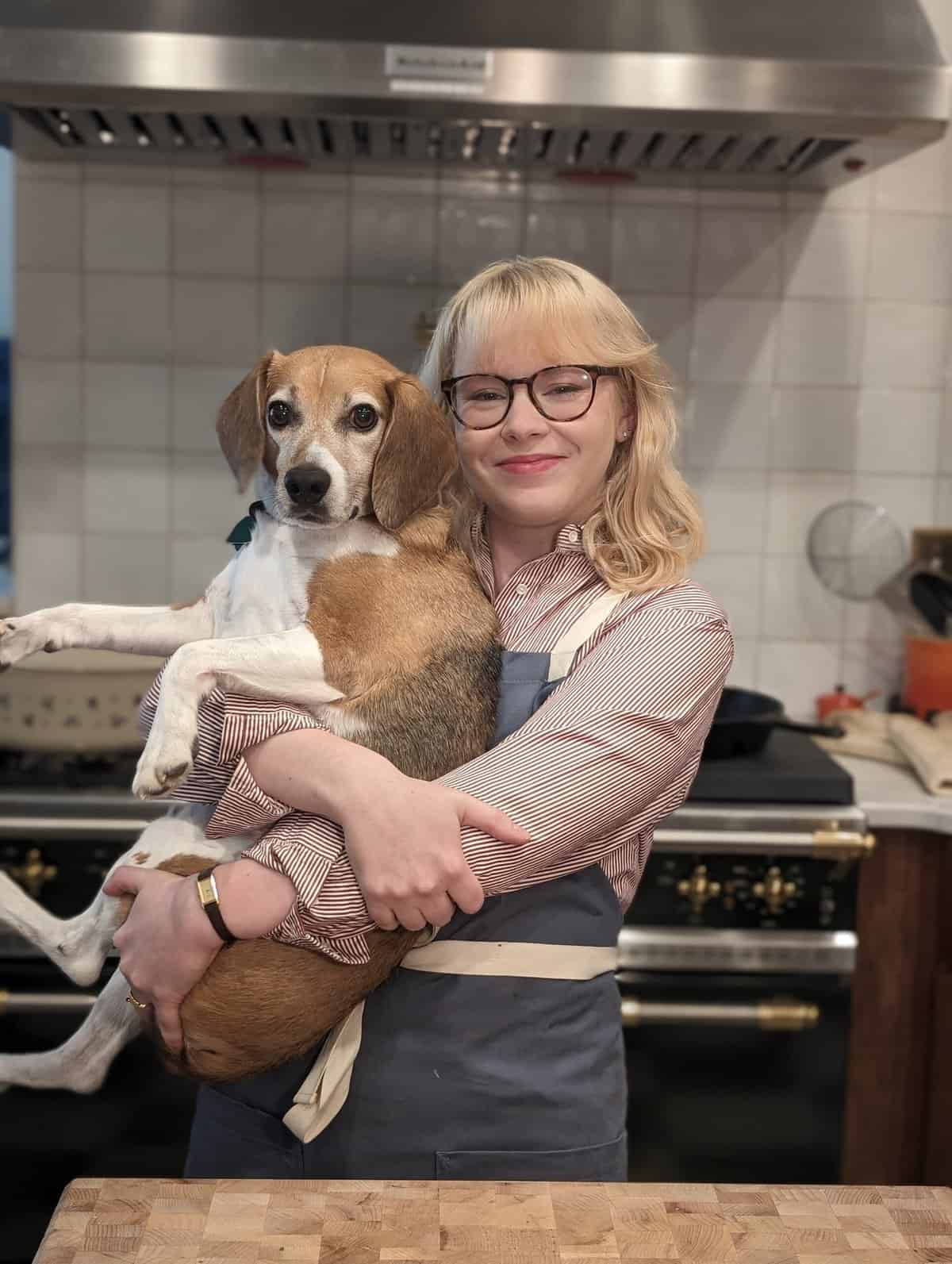 A woman holding a dog in a kitchen.