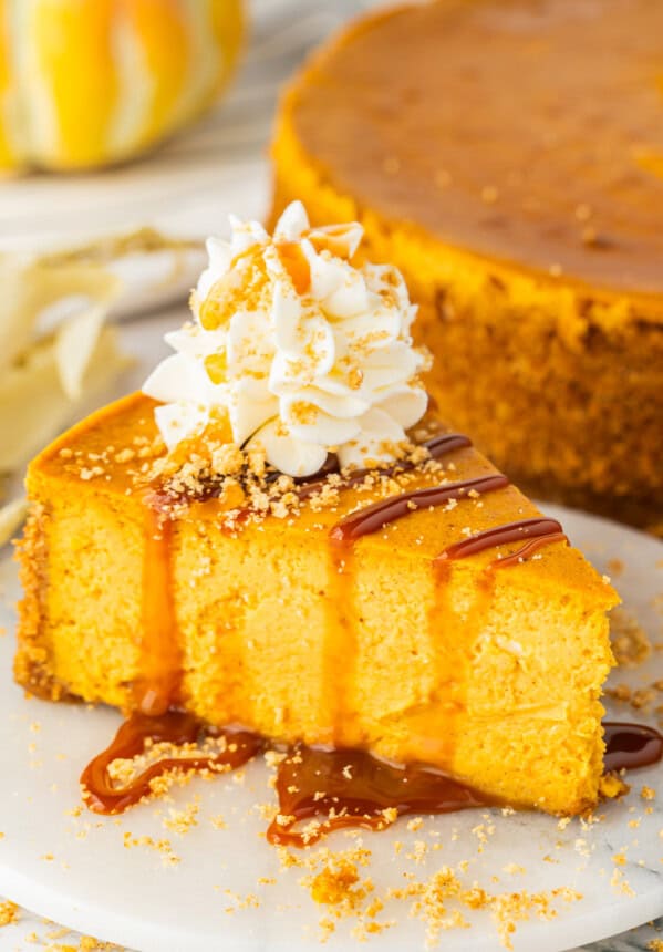 a slice of pumpkin cheesecake drizzled with caramel and whipped cream on a white plate.