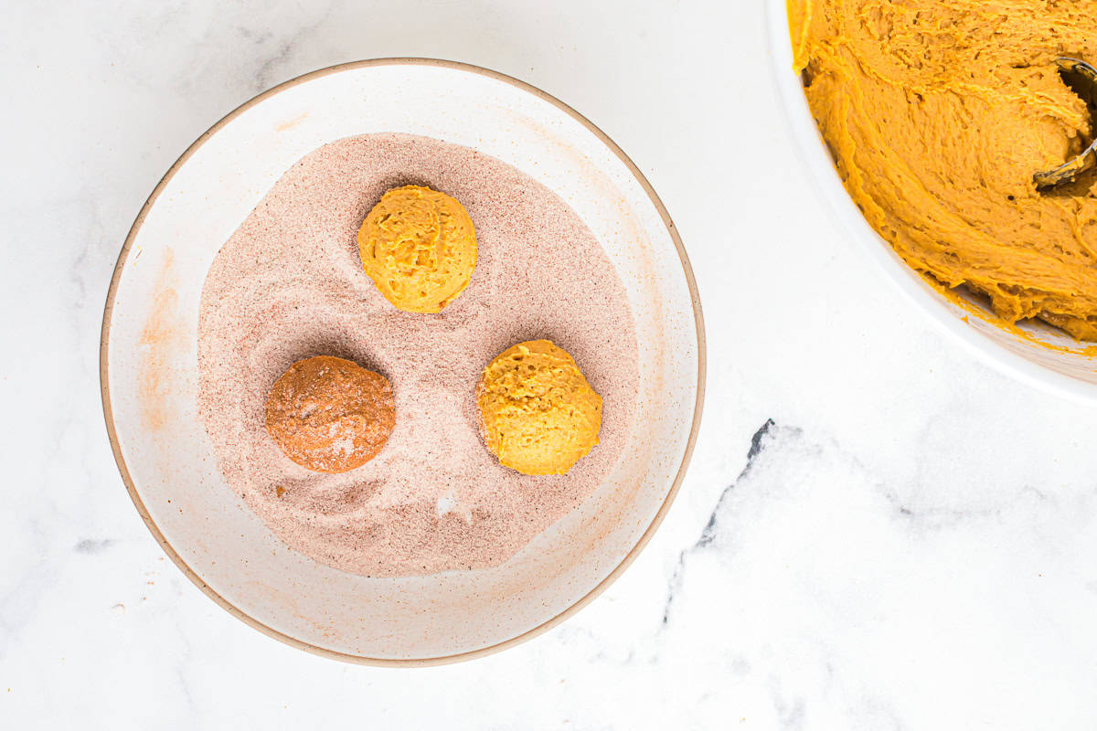 rolling pumpkin snickerdoodle cookie dough balls in spiced sugar.