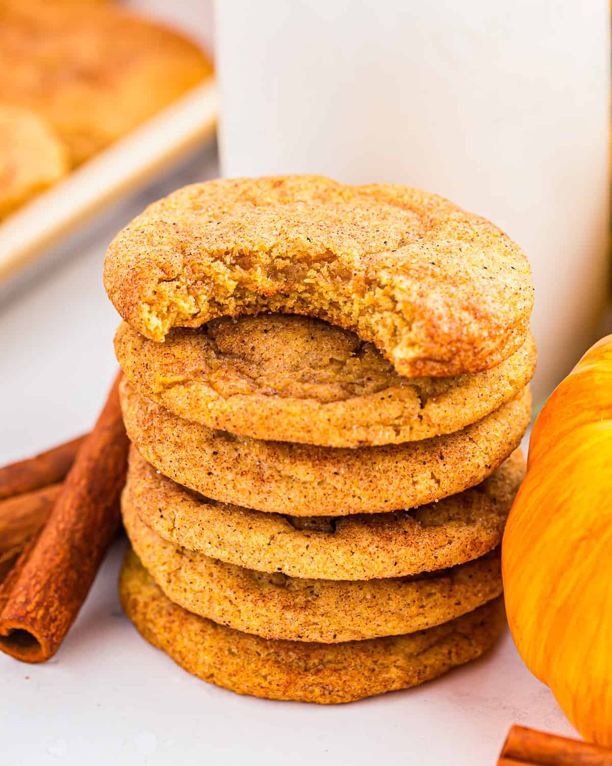 a bitten pumpkin snickerdoodle cookie on top of a stack of cookies.