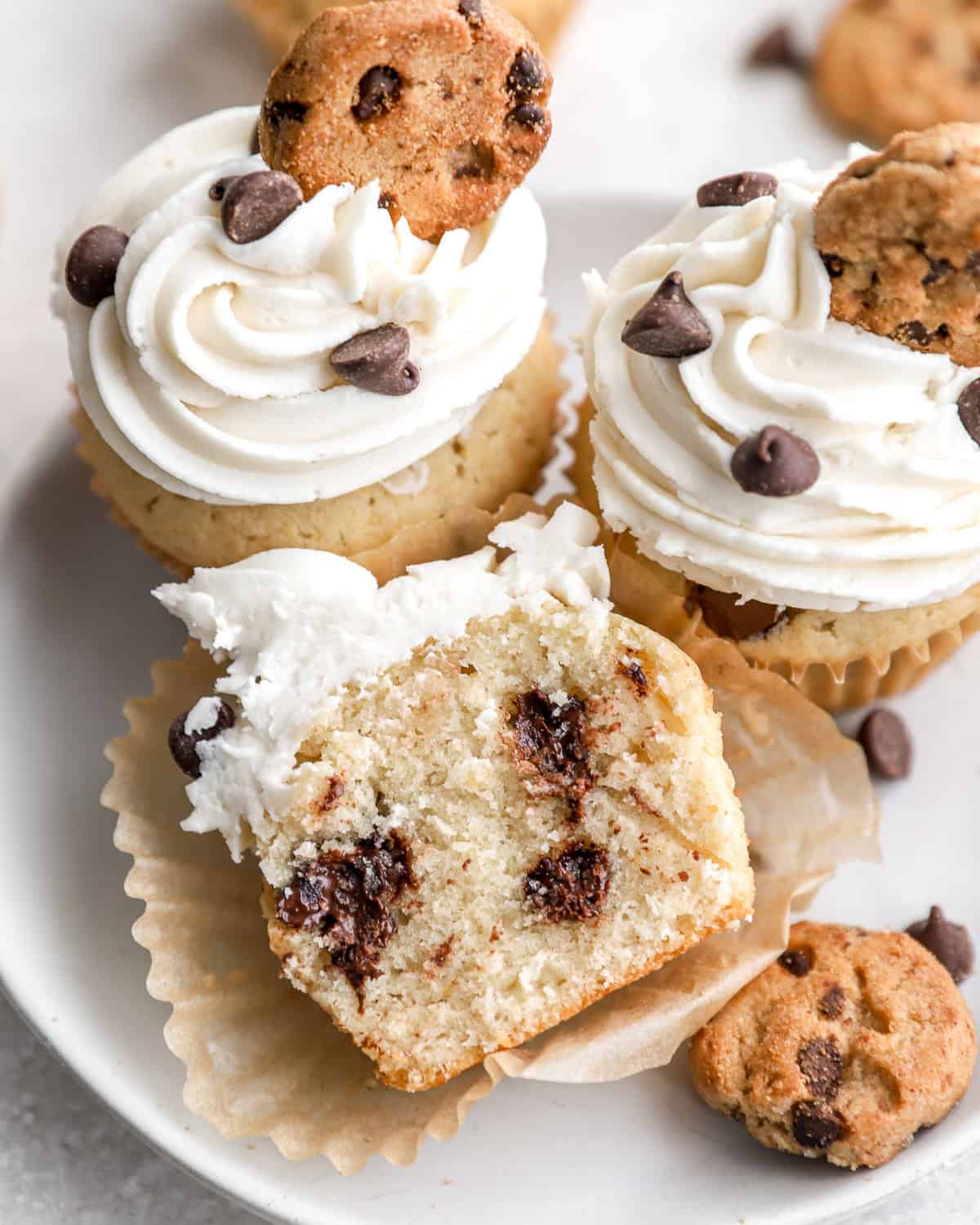 Three chocolate chip cookie cupcakes on a plate; one is unwrapped and cut in half.