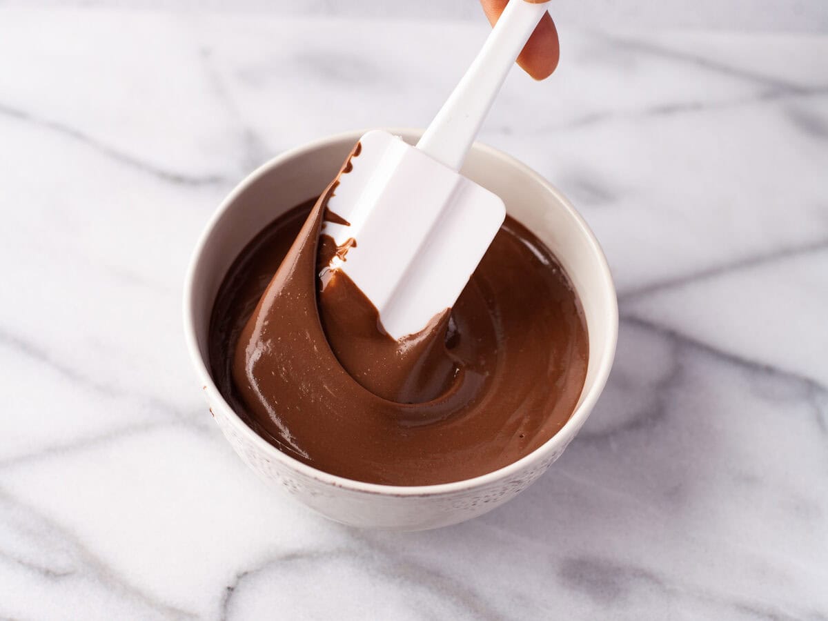 Rubber spatula stirring melted chocolate in a bowl.