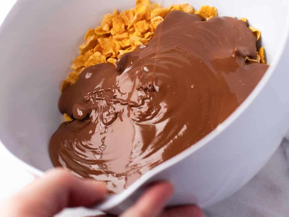 Pouring melted chocolate chips into a bowl of cornflakes.