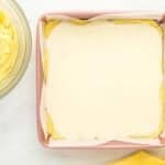 cream cheese filling spread over lemon cake batter in a square baking pan.