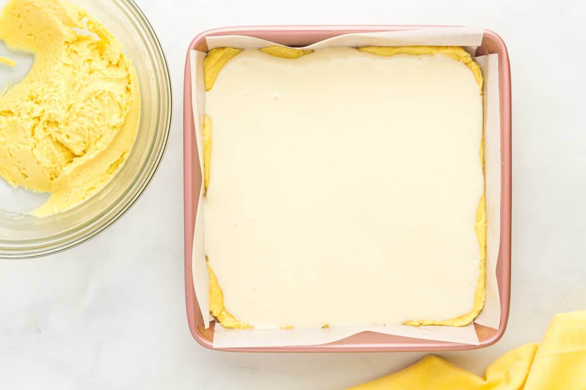 cream cheese filling spread over lemon cake batter in a square baking pan.