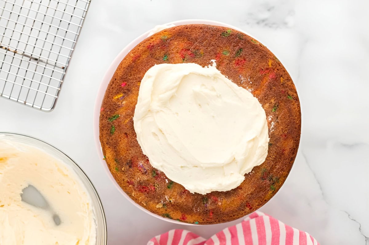 a fruity pebbles cake layer with frosting on top on a cake stand.