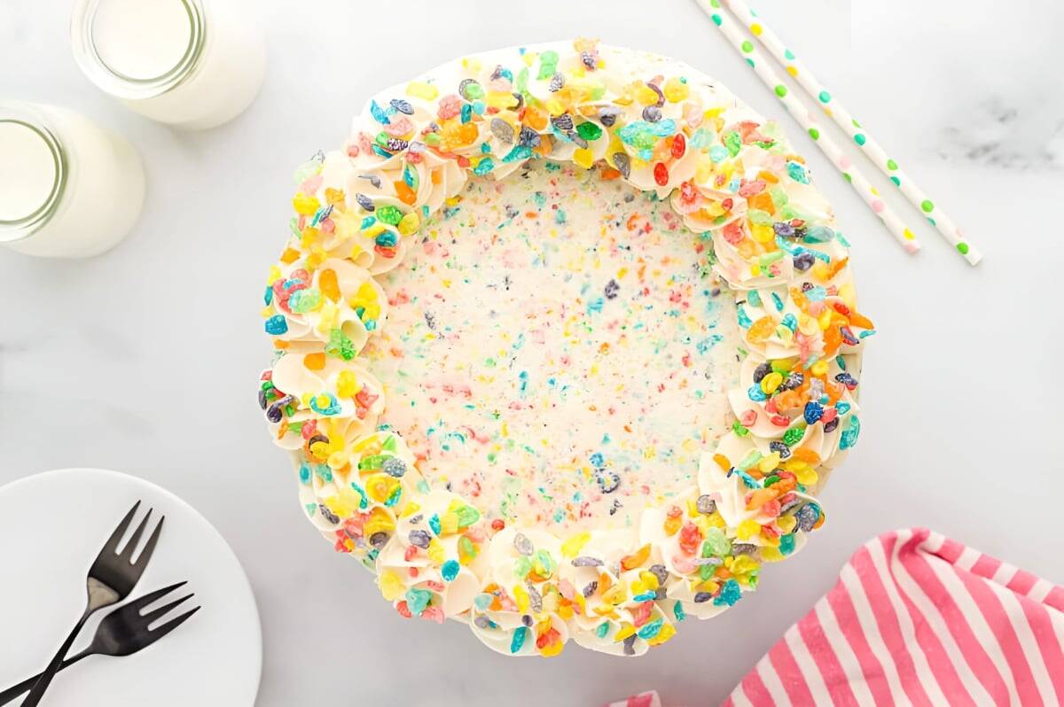a frosted fruity pebbles cake decorated with cereal on a cake stand.