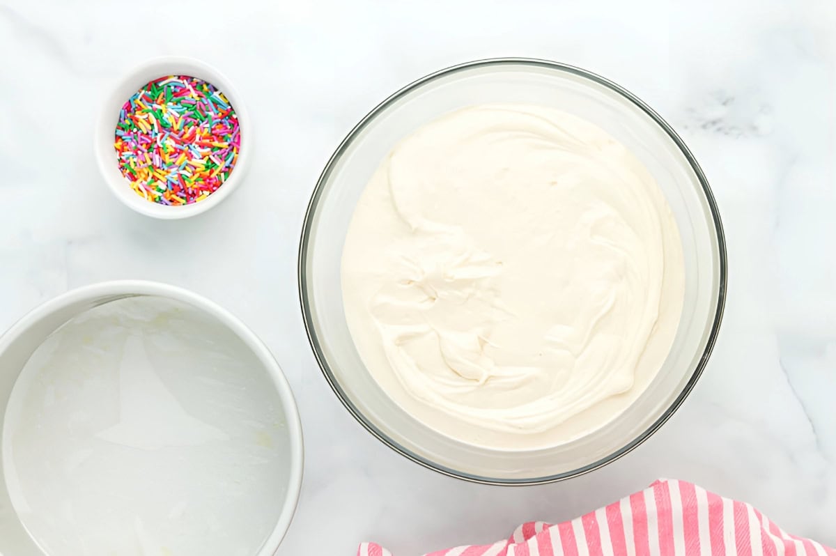 cake batter in a glass bowl next to a dish of sprinkles.