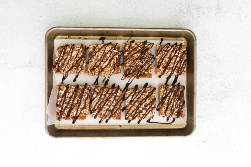 8 samoa cookie bars drizzled with chocolate on a lined baking sheet.