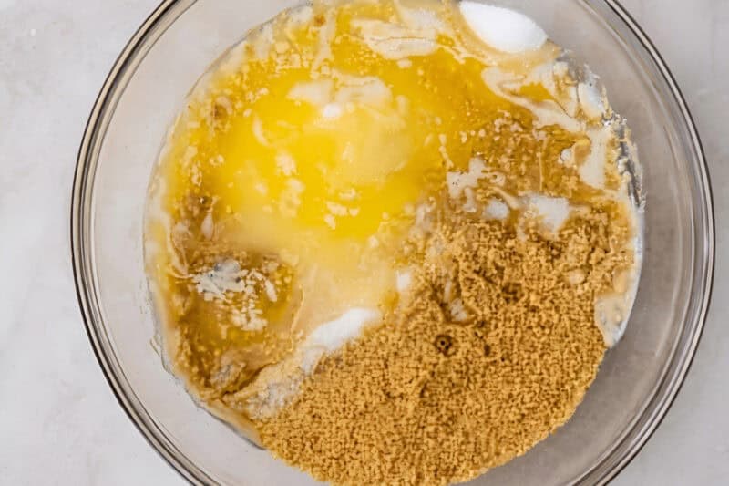 ingredients for graham cracker crust in a glass bowl: graham crackers, sugar, and melted butter.