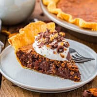 a slice of german chocolate pie topped with whipped cream and pecans on a plate with a fork.