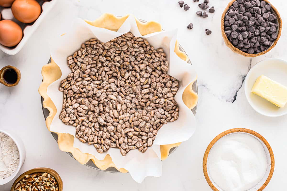 parchment paper and pie weights over a crimped pie crust in a pie pan.