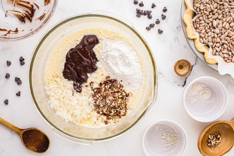 folding chocolate, coconut, pecans, and flour into whipped eggs in a glass bowl.