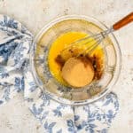 eggs, brown sugar, granulated sugar, melted butter, apple cider vinegar, vanilla, cinnamon, salt, and nutmeg in a glass bowl with a whisk.
