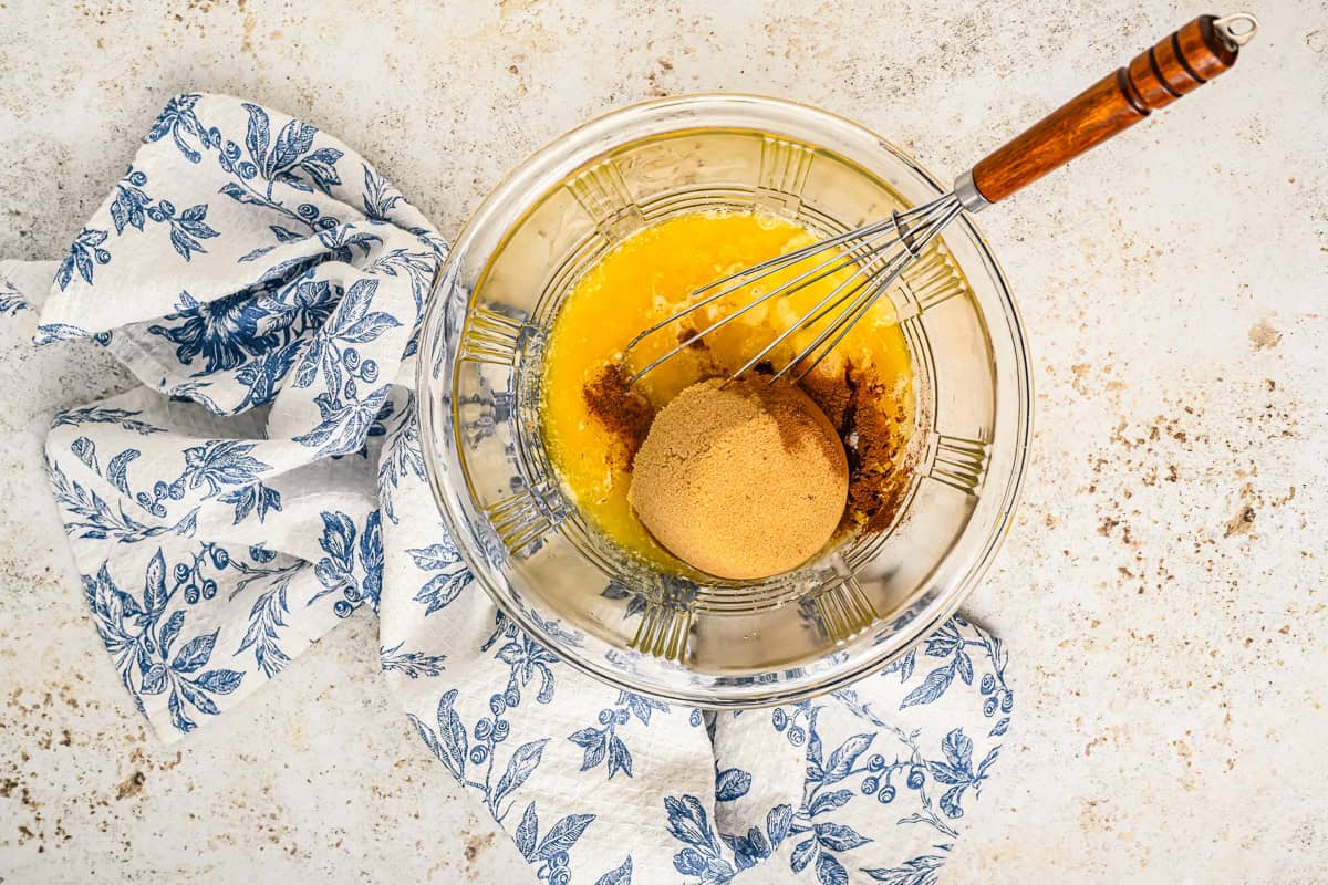 eggs, brown sugar, granulated sugar, melted butter, apple cider vinegar, vanilla, cinnamon, salt, and nutmeg in a glass bowl with a whisk.