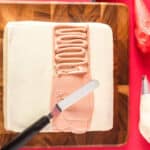spreading skin-tone frosting on santa cake in a wide strip with an offset spatula.