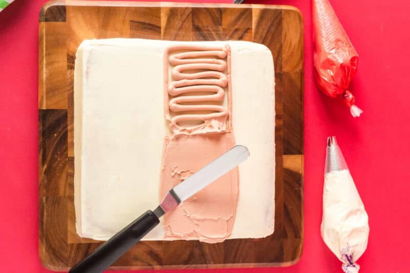 spreading skin-tone frosting on santa cake in a wide strip with an offset spatula.