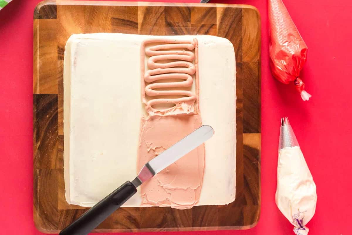 spreading skin-tone frosting on santa cake in a wide strip with an offset spatula.